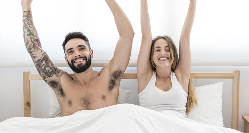 Couple souriant et s'&eacute;tirant dans un lit apr&egrave;s une nuit relaxante