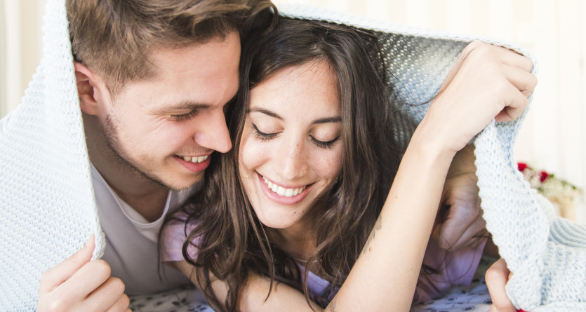 Couple souriant sous une couverture, partageant un moment intime et complice