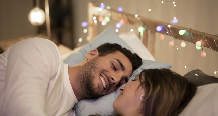 Couple souriant allong&eacute; dans un lit d&eacute;cor&eacute; de guirlandes lumineuses
