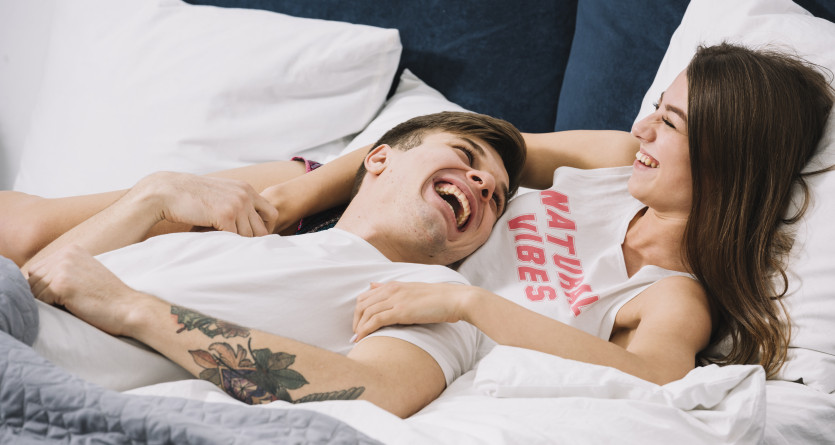 Couple allong&eacute; dans un lit, riant ensemble et profitant d'un moment complice