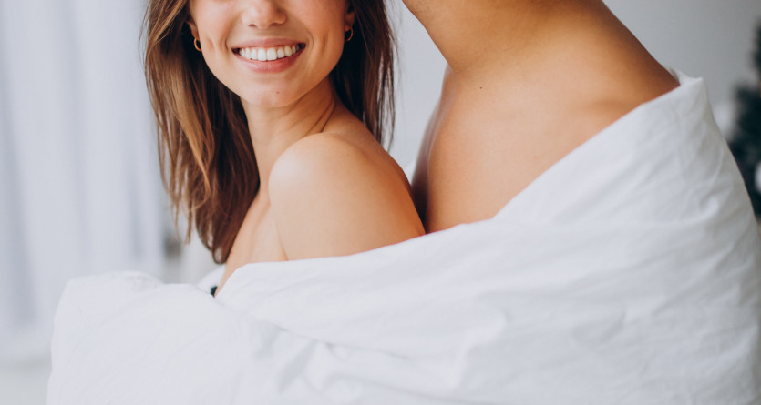 Couple complice partageant un moment intime sous une couverture dans une chambre romantique