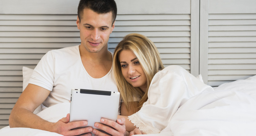 Couple dans une Love Room, relaxant ensemble en regardant une tablette dans un lit confortable