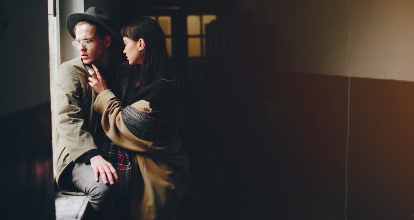Couple se tenant dans un couloir sombre, partageant un moment complice et intime